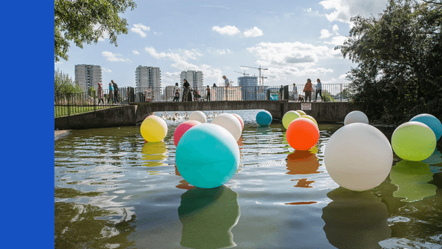 Colourful floating circles on water, with people walking in the background