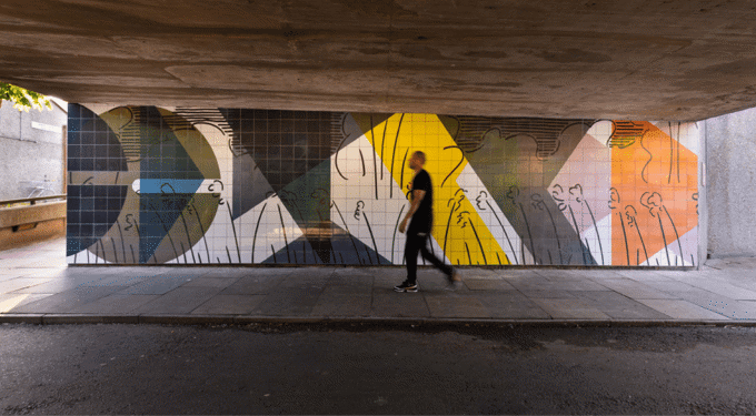 Man walking on the pavement next to a colourful wall