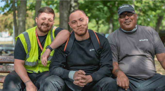 Three men sitting outside on a bench, smiling at the camera