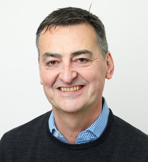 Headshot of a man in a dark grey jumper, smiling