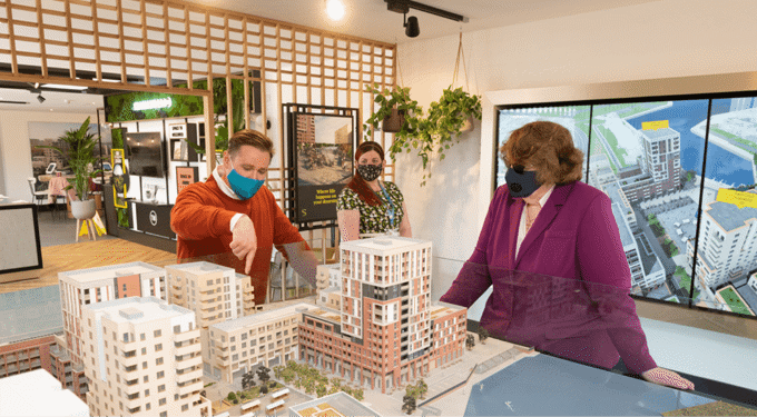 People wearing masks, looking at model of buildings