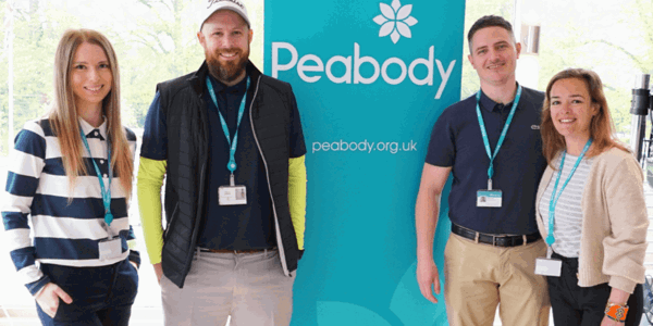 People smiling at the camera, while standing next to a Peabody sign