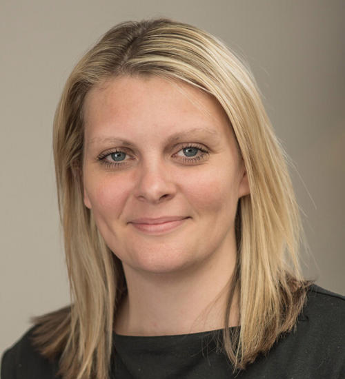 Headshot of a woman in a dark grey top, smiling