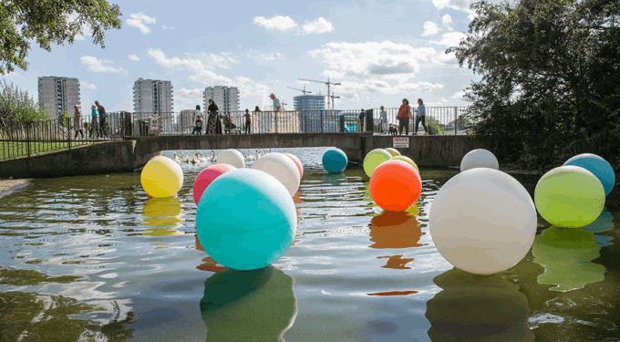 Colourful floating circles on water, with people walking in the background