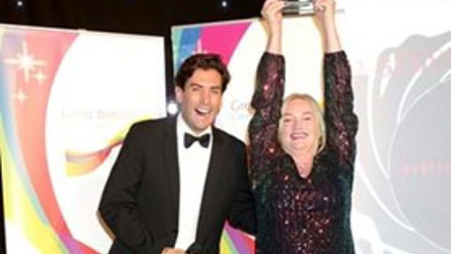 Man standing and smiling with a women holding an award above her head