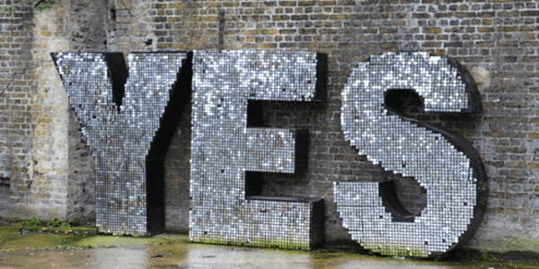 Big silver letters next to a brick wall spelling the word yes