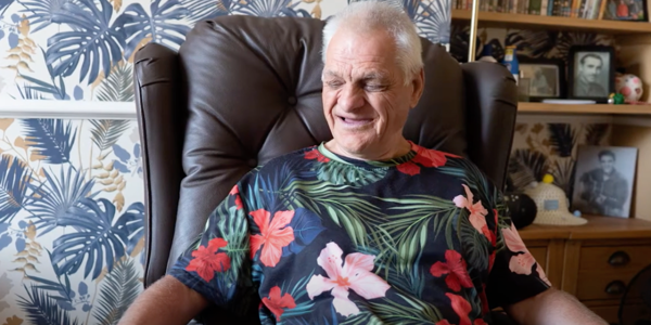 Man sitting in a brown chair, wearing a dark blue flowery patterned t-shirt