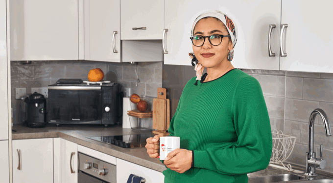 Woman wearing a green top, standing in a kitchen with a cup in her hand