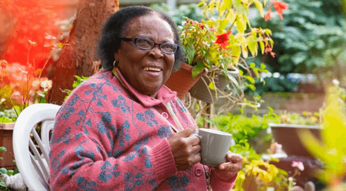 Woman wearing glasses, smiling at the camera and holding a cup